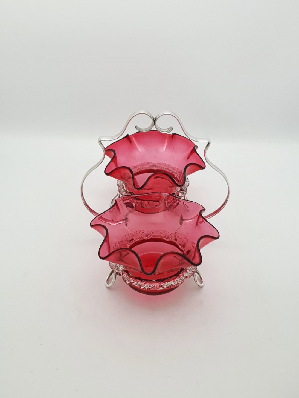 An Edwardian twin cranberry glass preserve dish set with crimped rims held in a silver-plated wireframe stand with a central handle. View VI