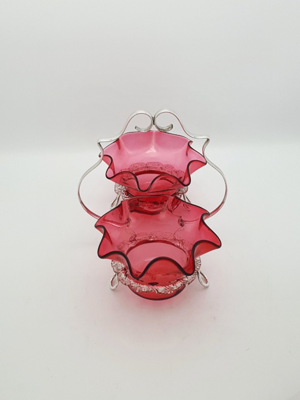 An Edwardian twin cranberry glass preserve dish set with crimped rims held in a silver-plated wireframe stand with a central handle. View VIII