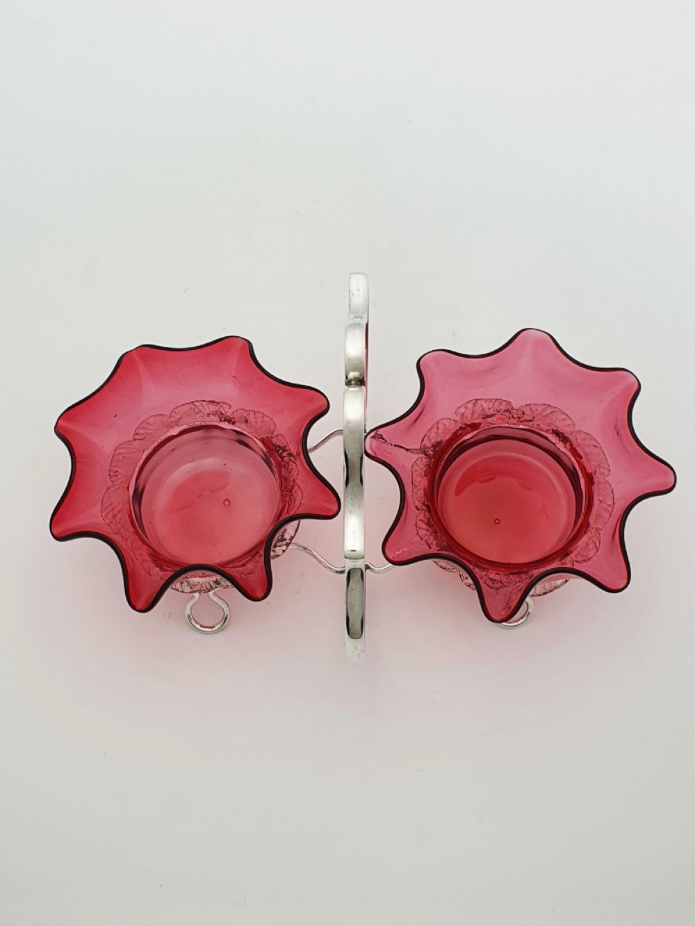 An Edwardian twin cranberry glass preserve dish set with crimped rims held in a silver-plated wireframe stand with a central handle. View IX
