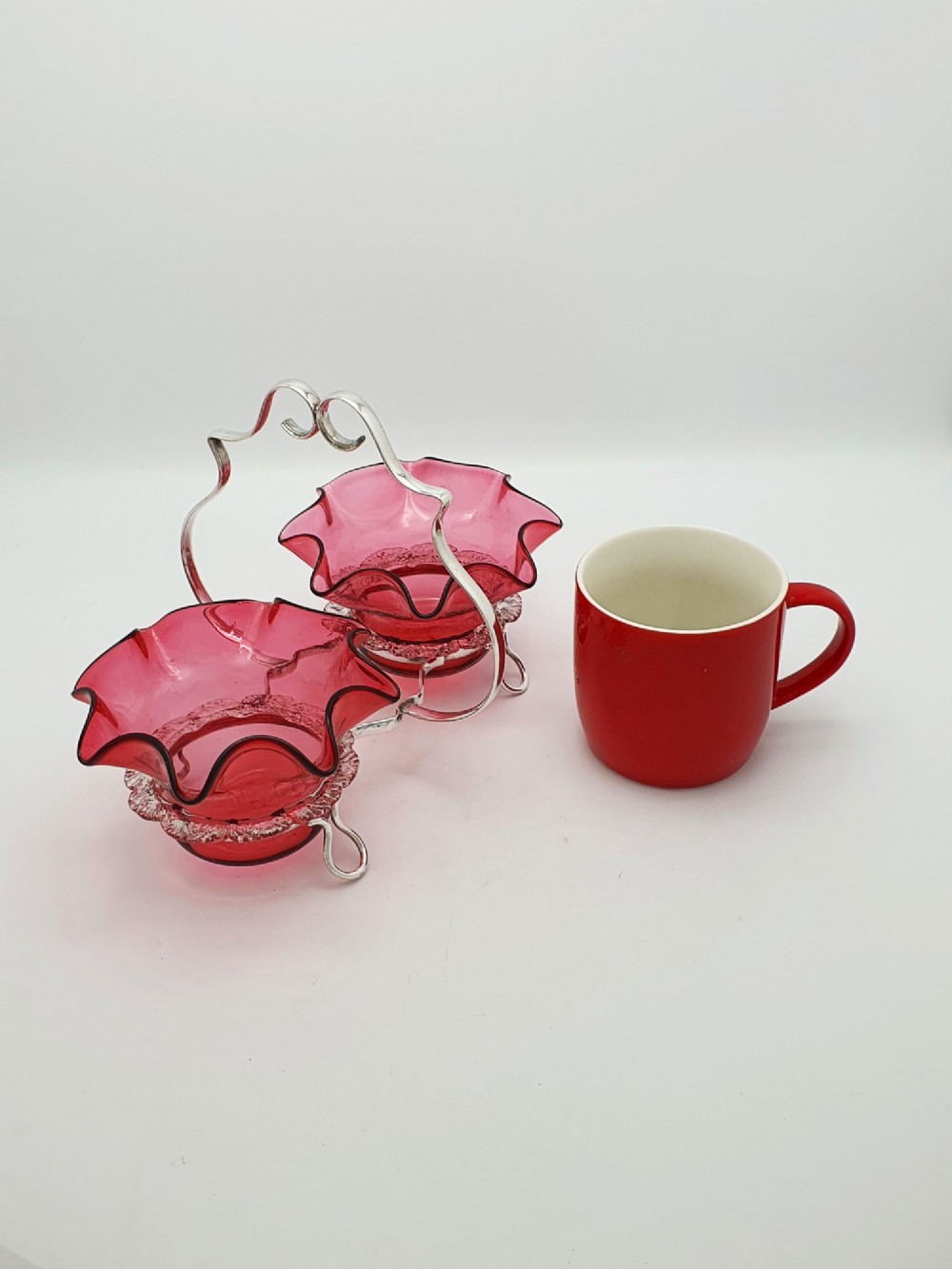 An Edwardian twin cranberry glass preserve dish set with crimped rims held in a silver-plated wireframe stand with a central handle. View XI