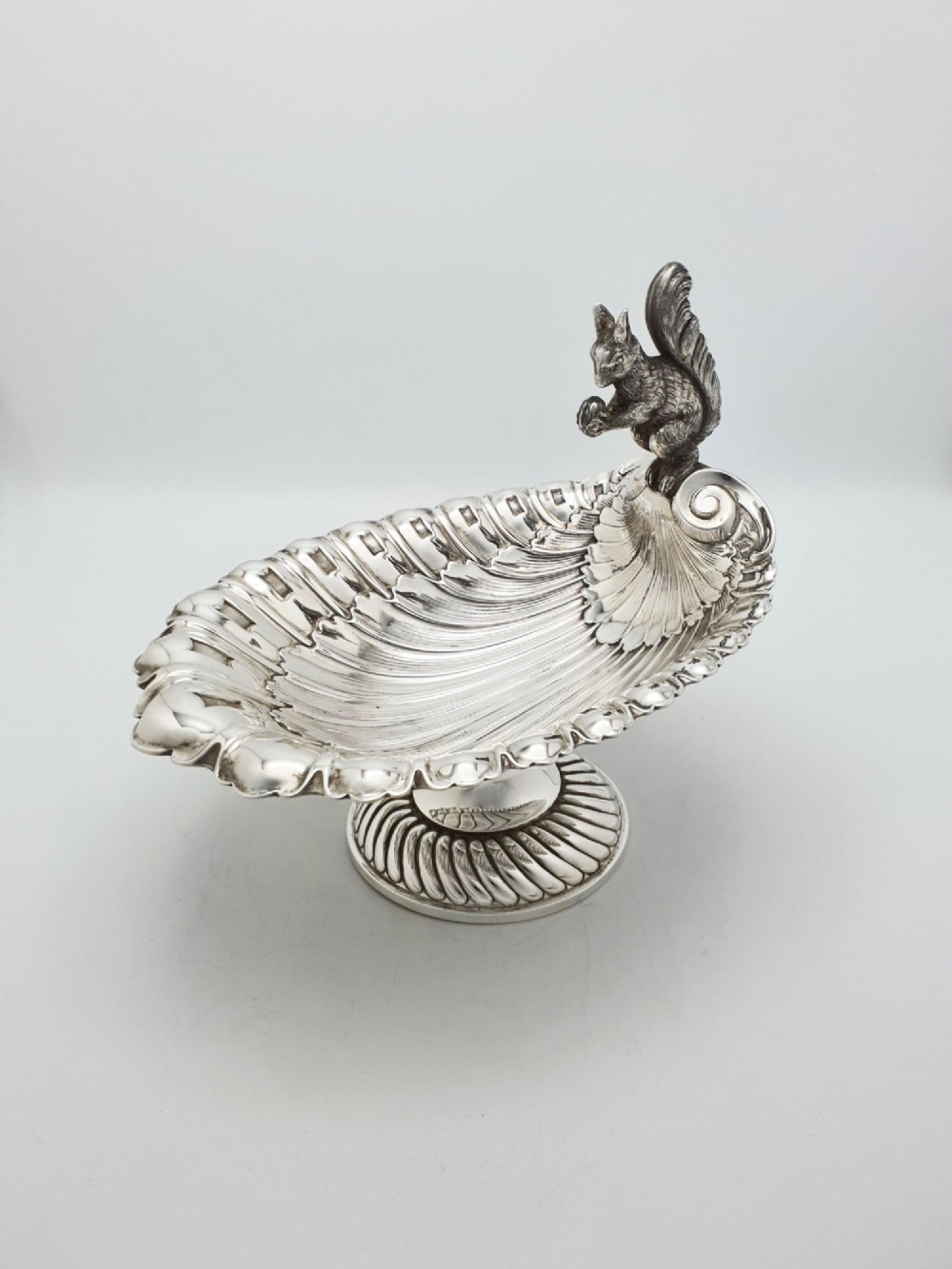 A silver-plated footed shell-shaped dish featuring a figurine of a squirrel perched on the rim holding an acorn, resting on a spiral-lobed pedestal base. View III