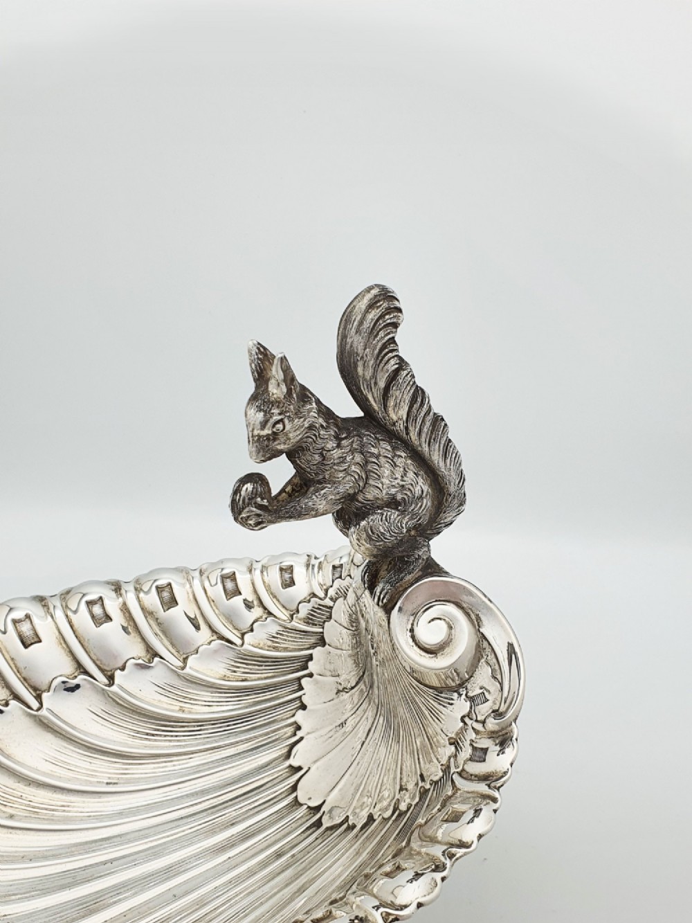 A silver-plated footed shell-shaped dish featuring a figurine of a squirrel perched on the rim holding an acorn, resting on a spiral-lobed pedestal base. View IV