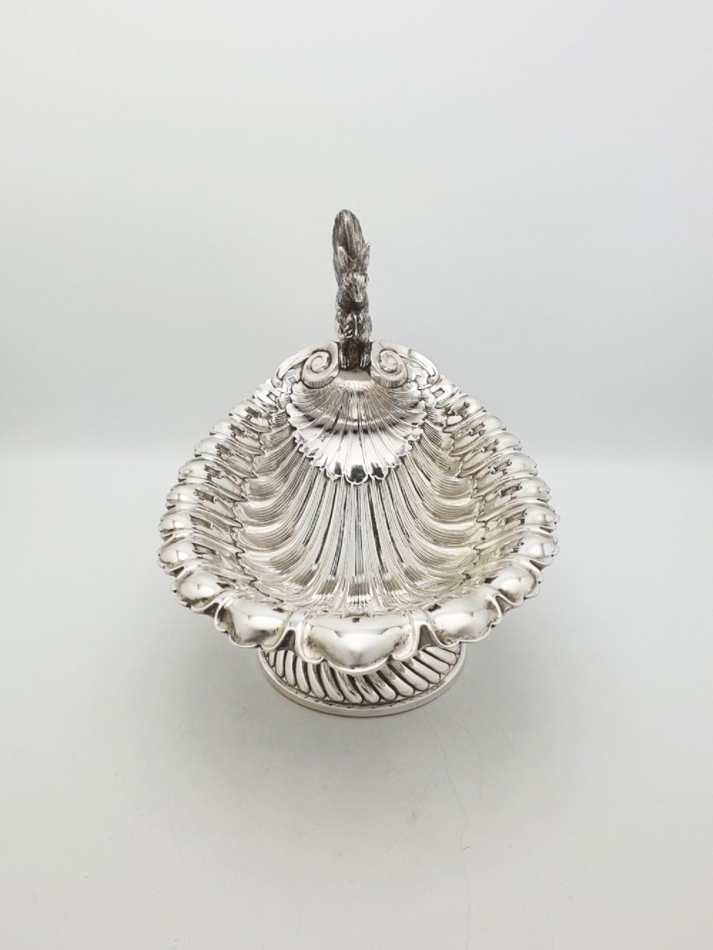 A silver-plated footed shell-shaped dish featuring a figurine of a squirrel perched on the rim holding an acorn, resting on a spiral-lobed pedestal base. View VI