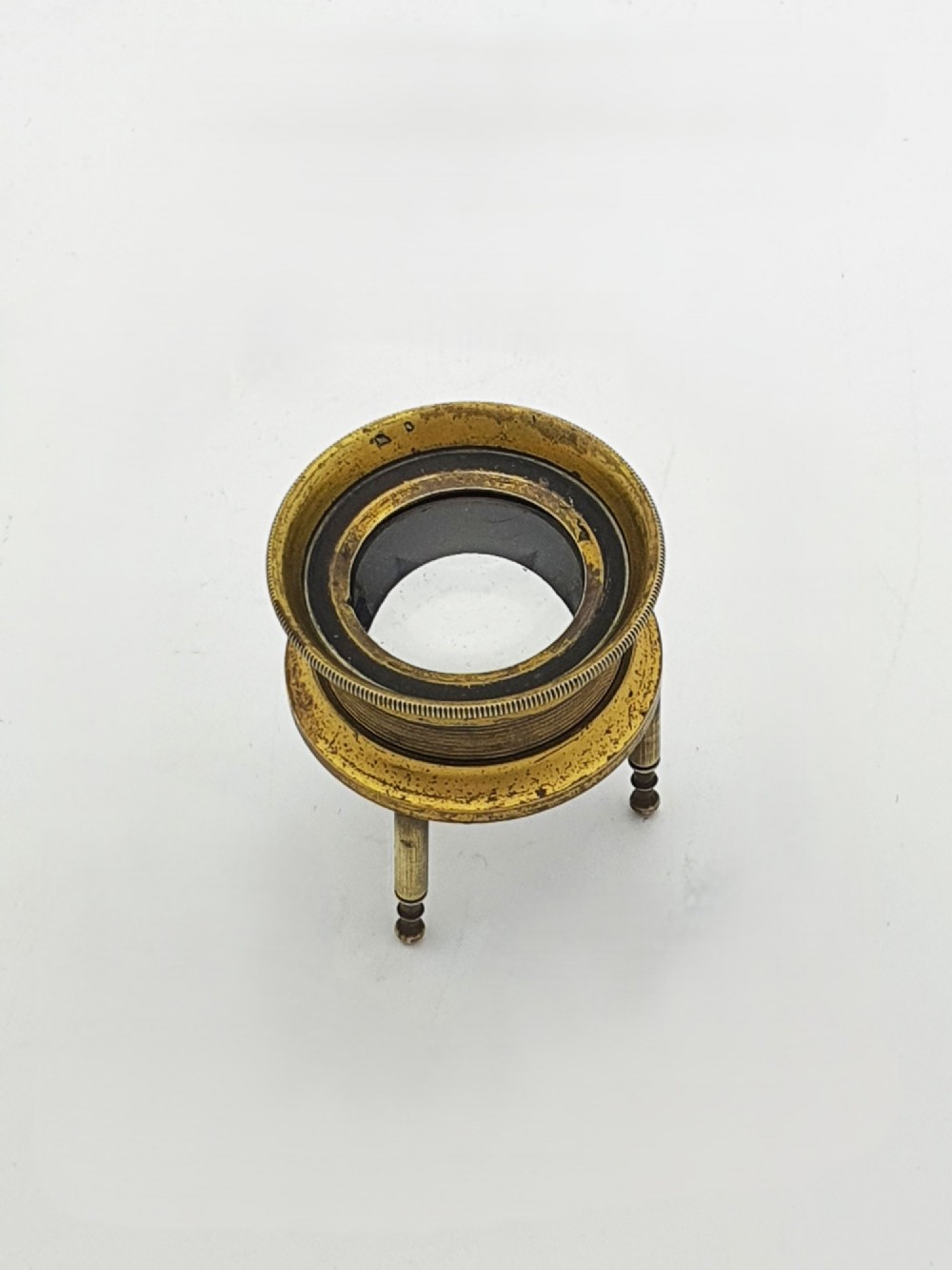 An antique Edwardian circular solid brass desk magnifying loupe resting on three turned tripod feet.