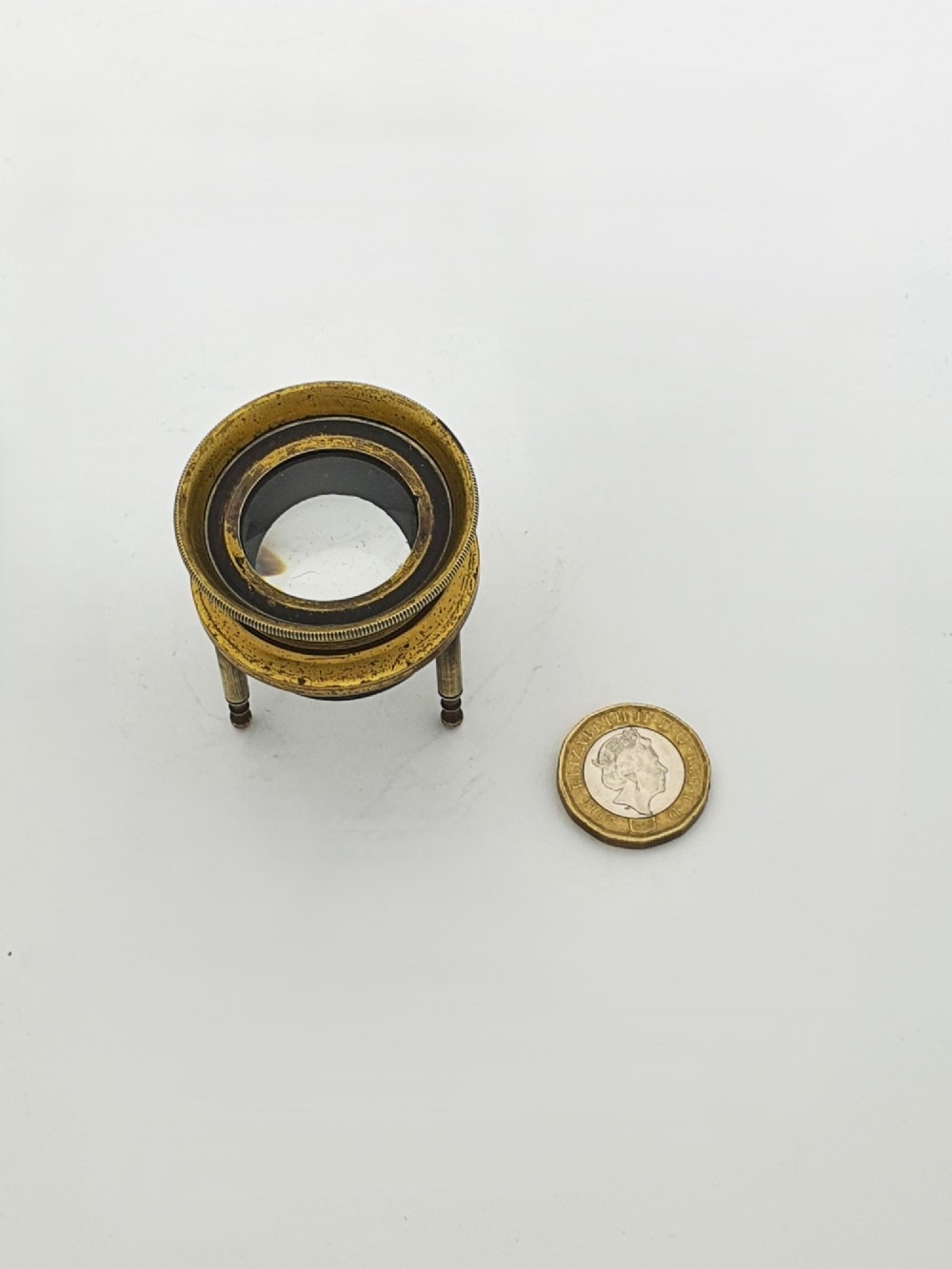 An antique Edwardian circular solid brass desk magnifying loupe resting on three turned tripod feet. View V