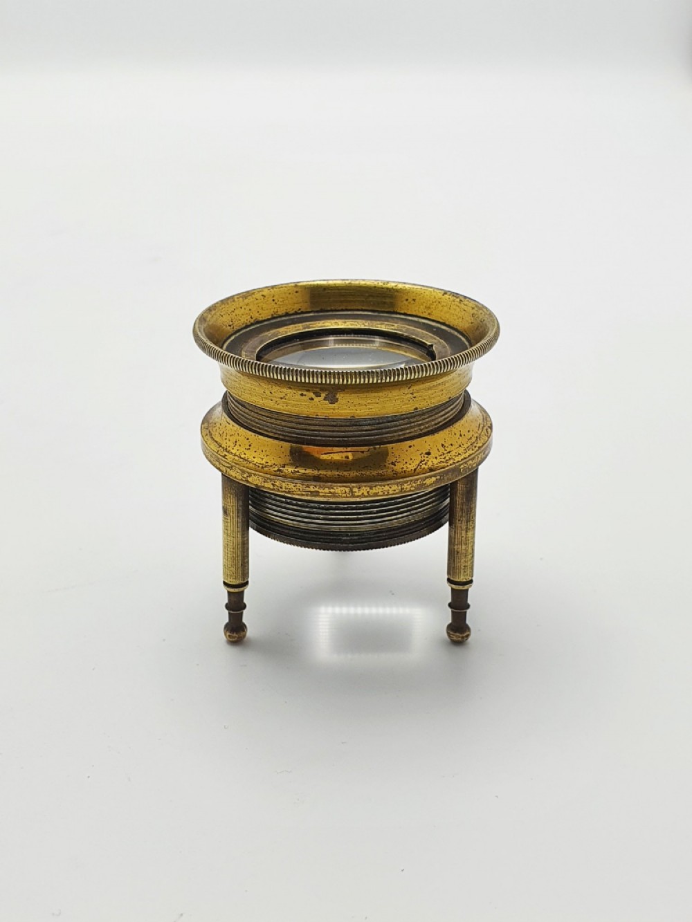 An antique Edwardian circular solid brass desk magnifying loupe resting on three turned tripod feet. View VI