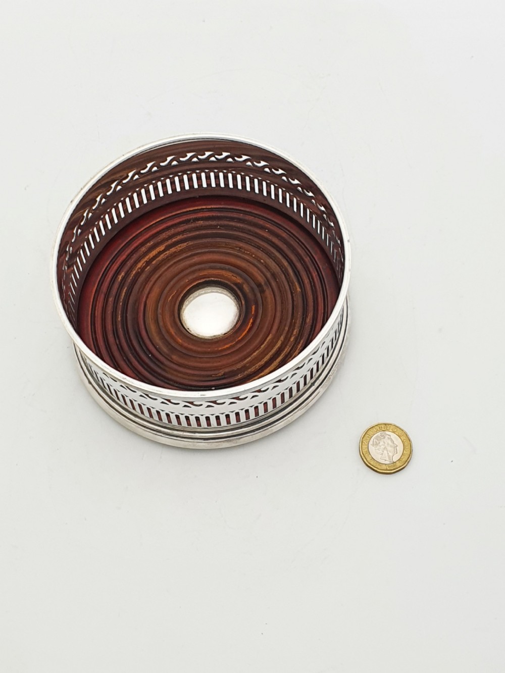 A pair of circular silver plated wine coasters featuring pierced fretwork sides, turned mahogany bases with central silver bosses, and dark felt underneath. View V