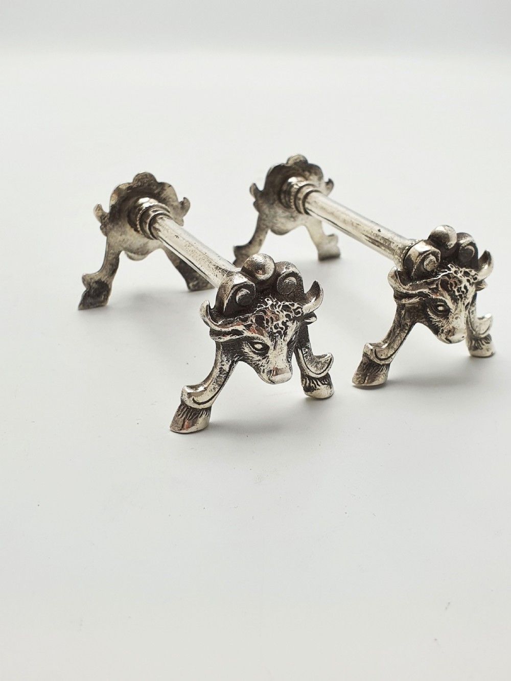 A pair of Victorian silver-plated knife rests featuring detailed cast bull head terminals with hoof legs supporting a cylindrical bar.