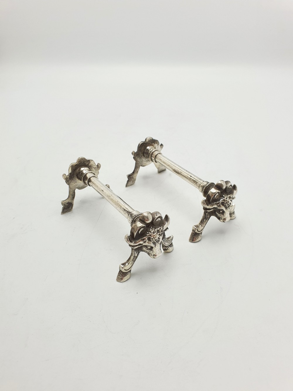 A pair of Victorian silver-plated knife rests featuring detailed cast bull head terminals with hoof legs supporting a cylindrical bar. View II