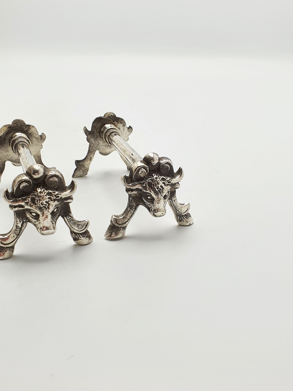 A pair of Victorian silver-plated knife rests featuring detailed cast bull head terminals with hoof legs supporting a cylindrical bar. View III