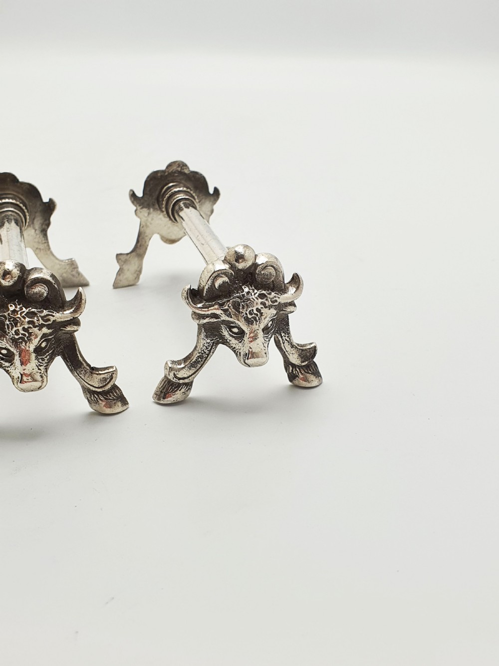 A pair of Victorian silver-plated knife rests featuring detailed cast bull head terminals with hoof legs supporting a cylindrical bar. View V