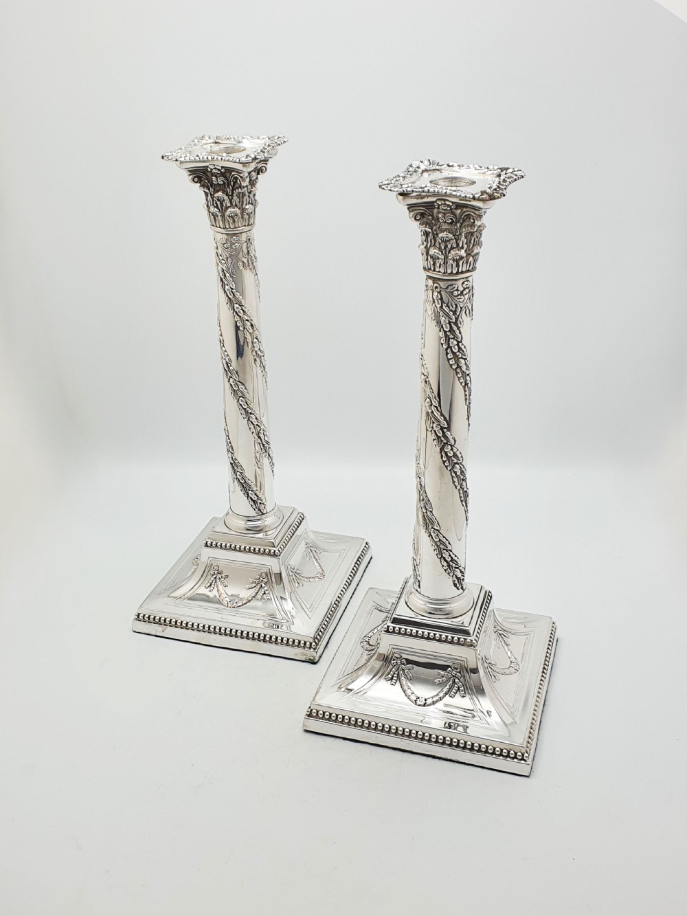 A pair of Victorian silver-plated candlesticks designed as Neoclassical Corinthian columns with spiral floral garlands and square beaded bases.