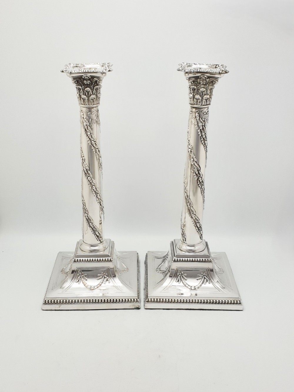 A pair of Victorian silver-plated candlesticks designed as Neoclassical Corinthian columns with spiral floral garlands and square beaded bases. View II
