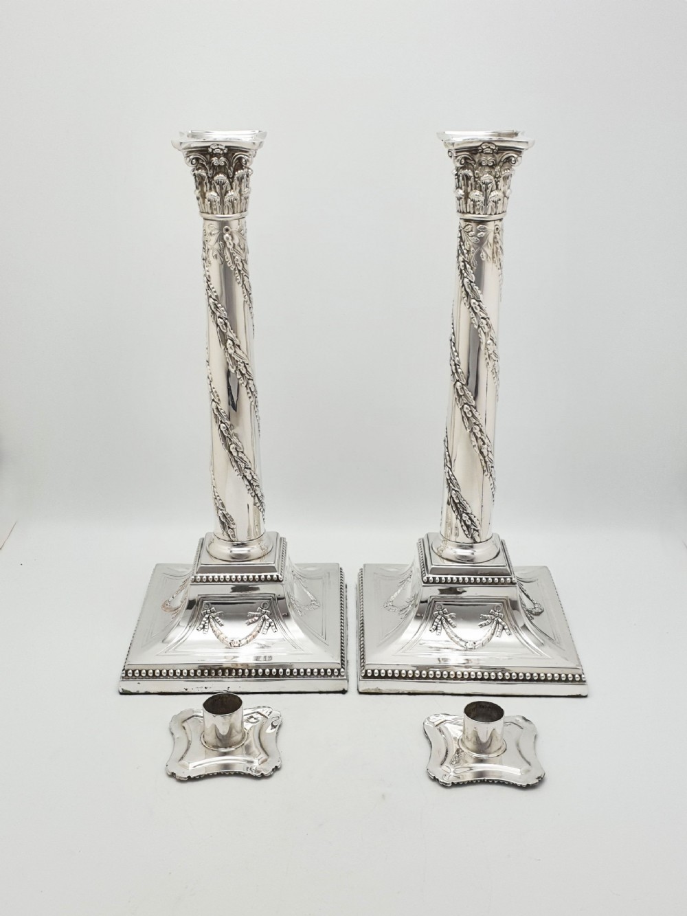 A pair of Victorian silver-plated candlesticks designed as Neoclassical Corinthian columns with spiral floral garlands and square beaded bases. View IV