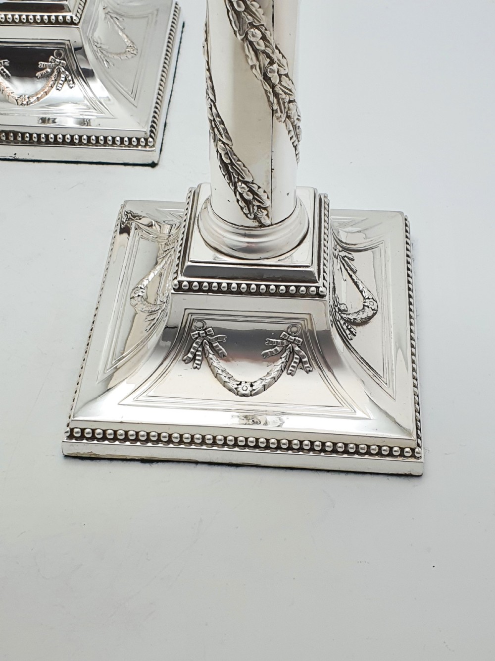 A pair of Victorian silver-plated candlesticks designed as Neoclassical Corinthian columns with spiral floral garlands and square beaded bases. View VII