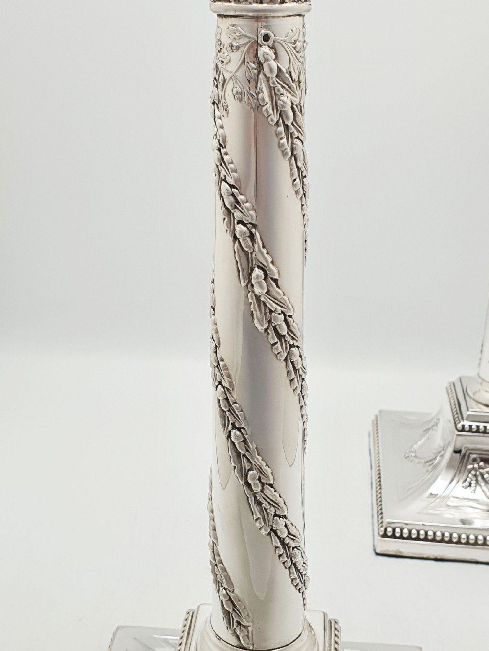 A pair of Victorian silver-plated candlesticks designed as Neoclassical Corinthian columns with spiral floral garlands and square beaded bases. View X