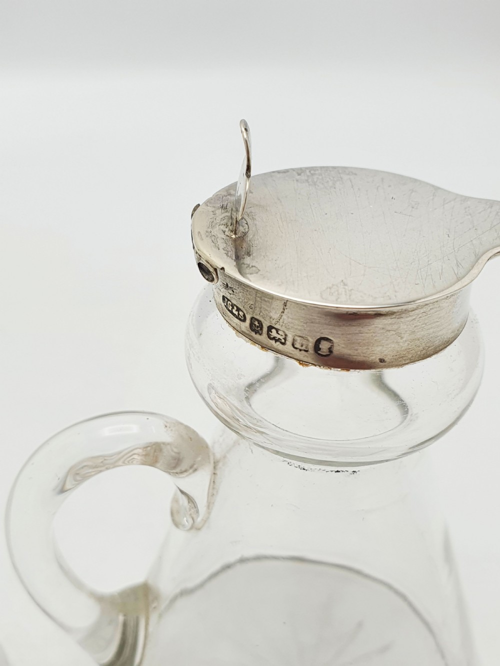 A pair of clear glass conical whiskey noggins with sterling silver collars, hinged lids, and applied glass loop handles. View III