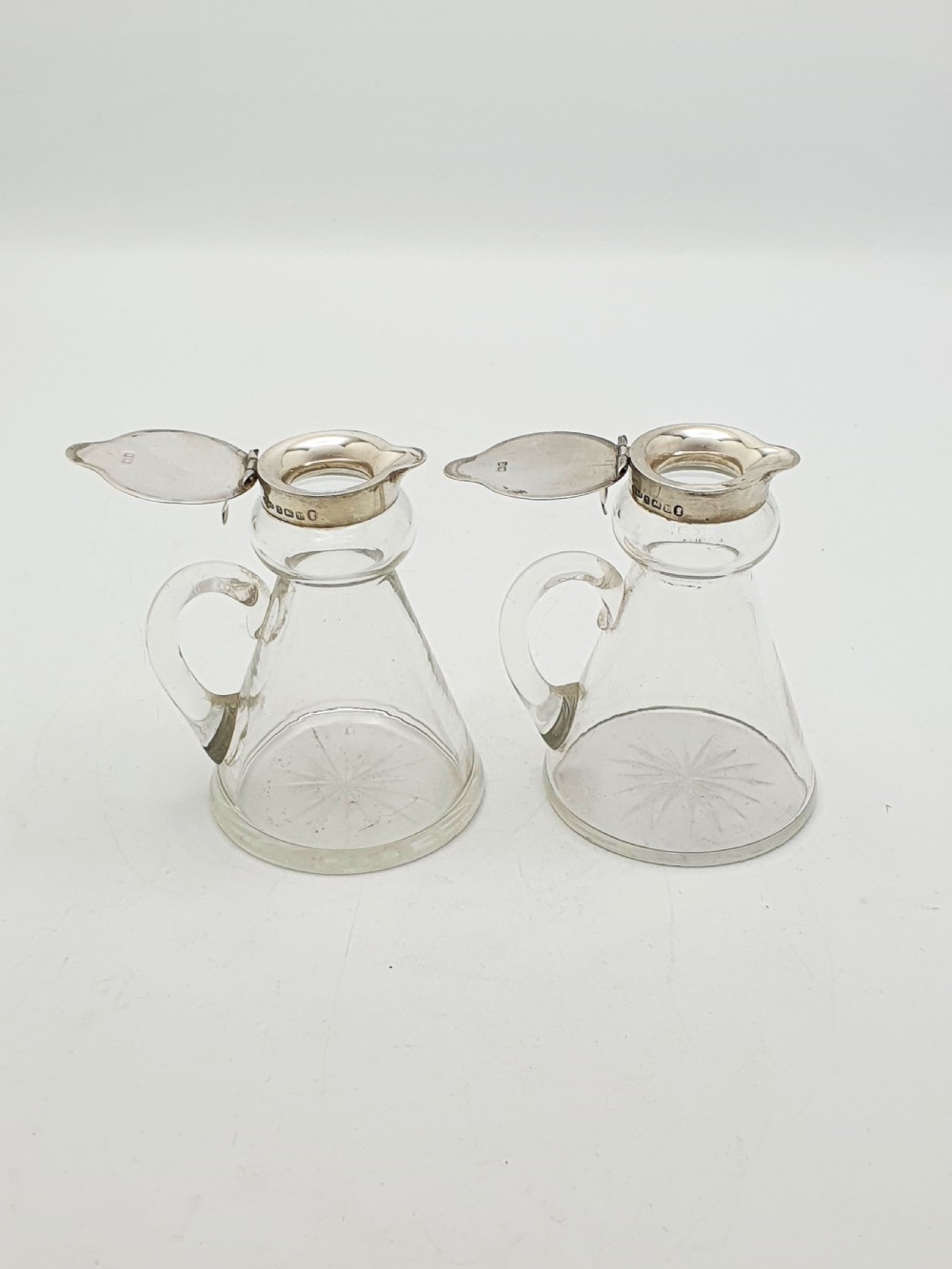 A pair of clear glass conical whiskey noggins with sterling silver collars, hinged lids, and applied glass loop handles. View IV