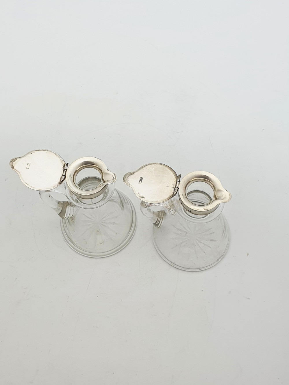 A pair of clear glass conical whiskey noggins with sterling silver collars, hinged lids, and applied glass loop handles. View V