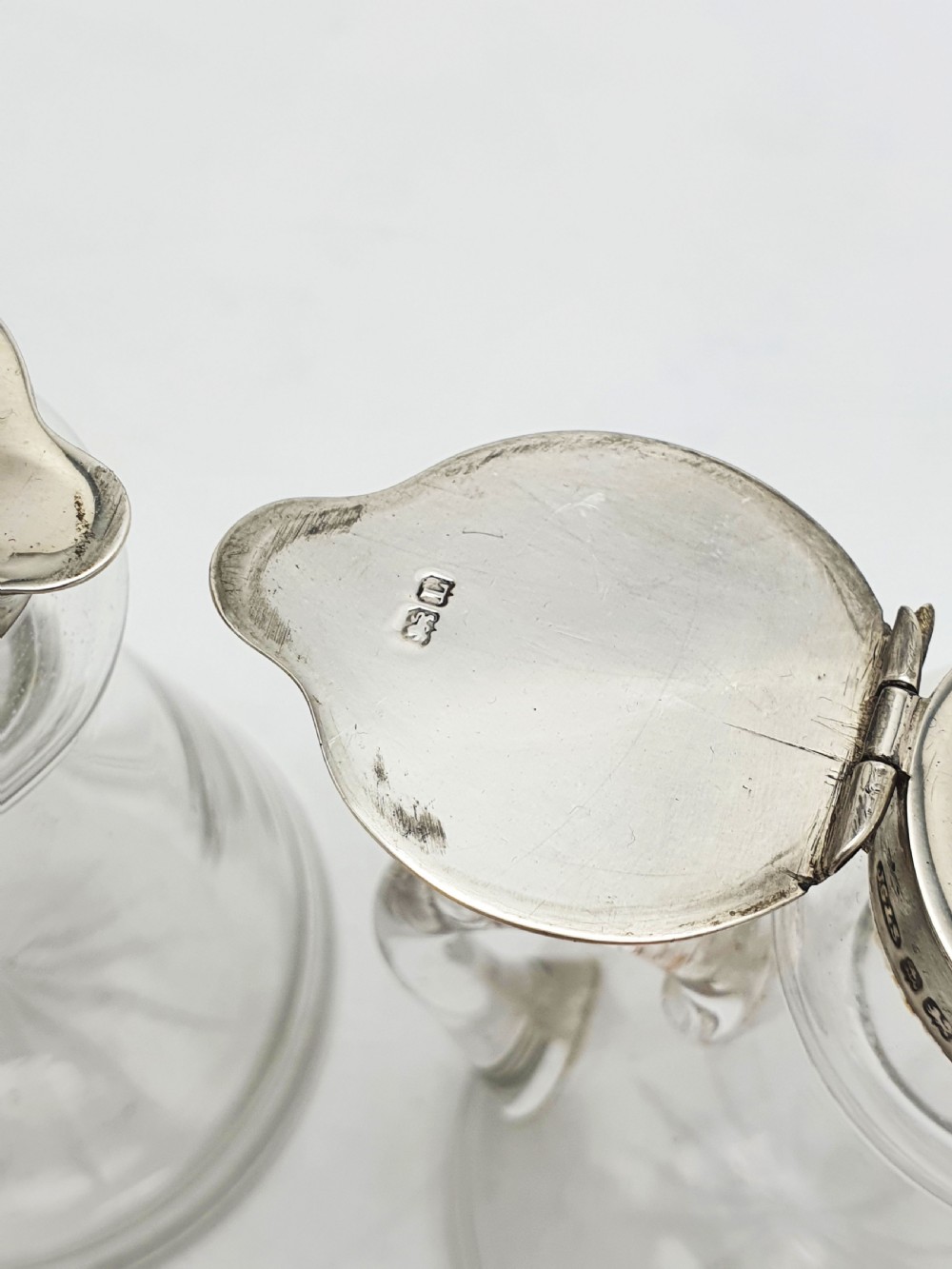 A pair of clear glass conical whiskey noggins with sterling silver collars, hinged lids, and applied glass loop handles. View VI