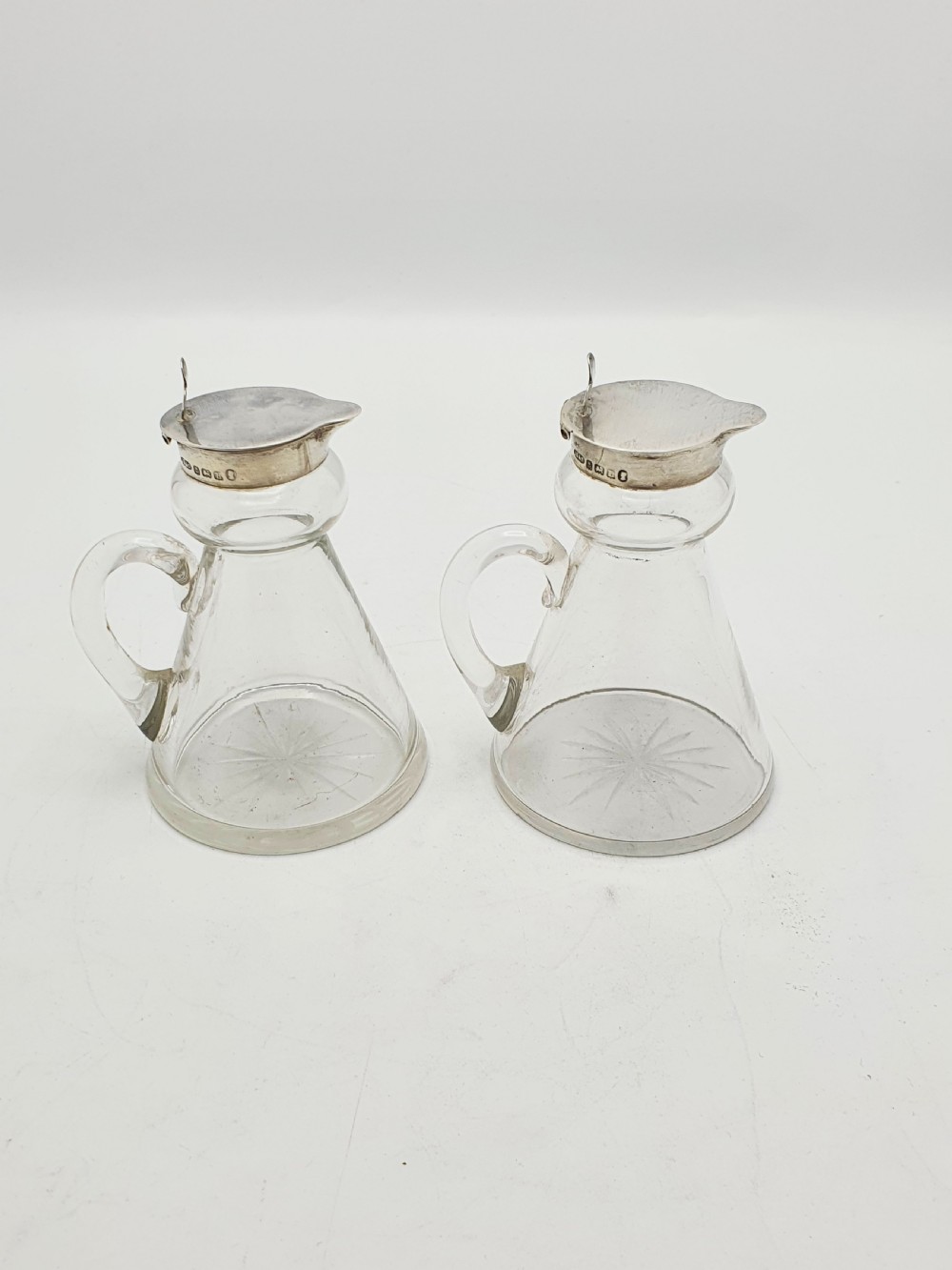 A pair of clear glass conical whiskey noggins with sterling silver collars, hinged lids, and applied glass loop handles. View XI
