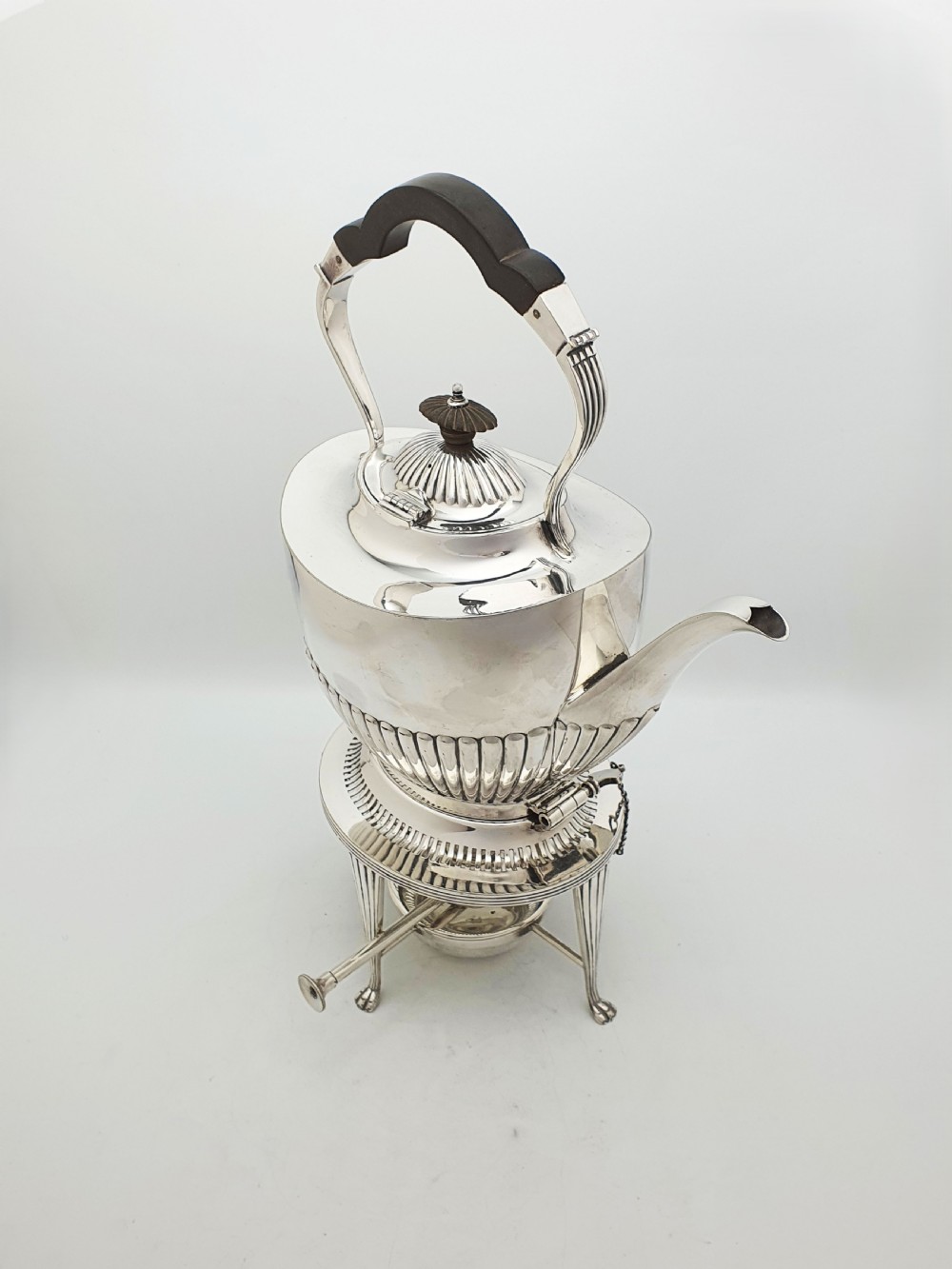 An Edwardian silver-plated spirit kettle featuring a half-fluted lower body, an ebony handle grip, and a matching tripod stand with an alcohol burner.