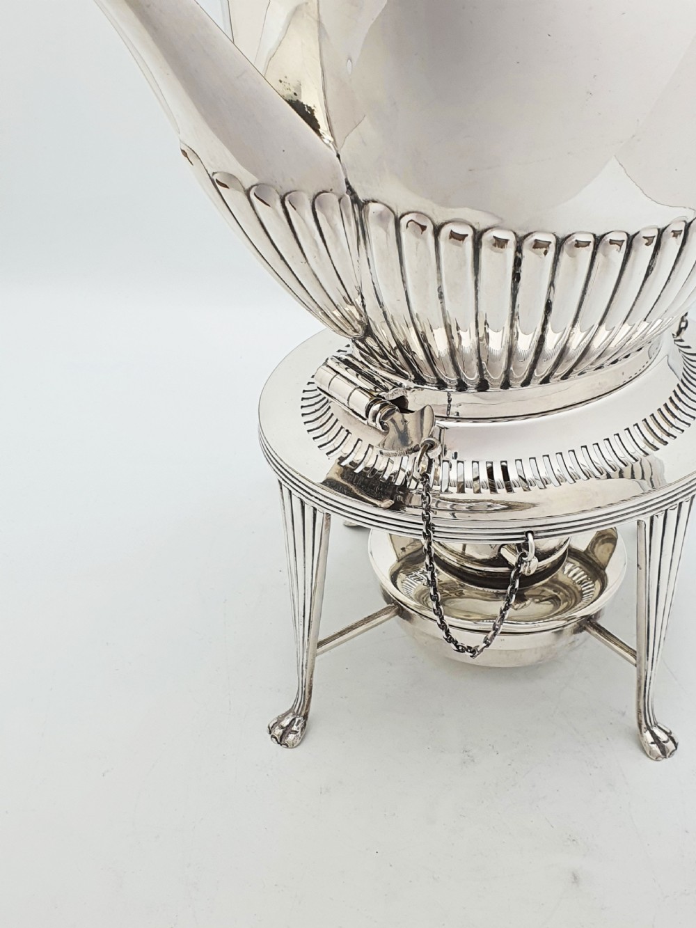 An Edwardian silver-plated spirit kettle featuring a half-fluted lower body, an ebony handle grip, and a matching tripod stand with an alcohol burner. View IV