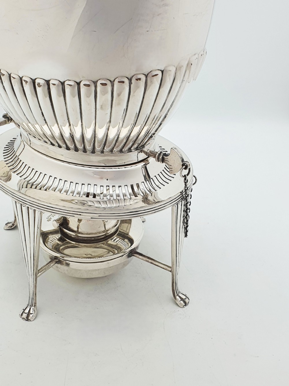 An Edwardian silver-plated spirit kettle featuring a half-fluted lower body, an ebony handle grip, and a matching tripod stand with an alcohol burner. View V