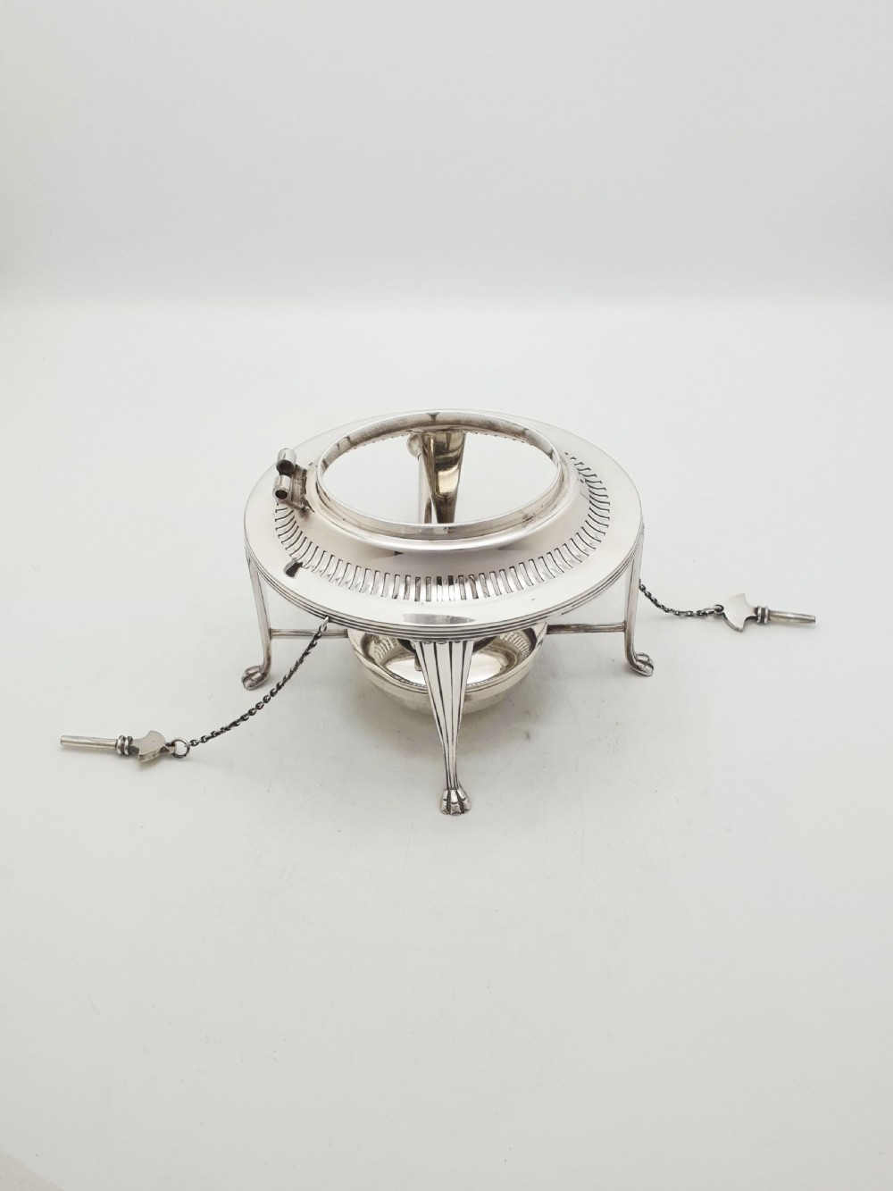 An Edwardian silver-plated spirit kettle featuring a half-fluted lower body, an ebony handle grip, and a matching tripod stand with an alcohol burner. View VI