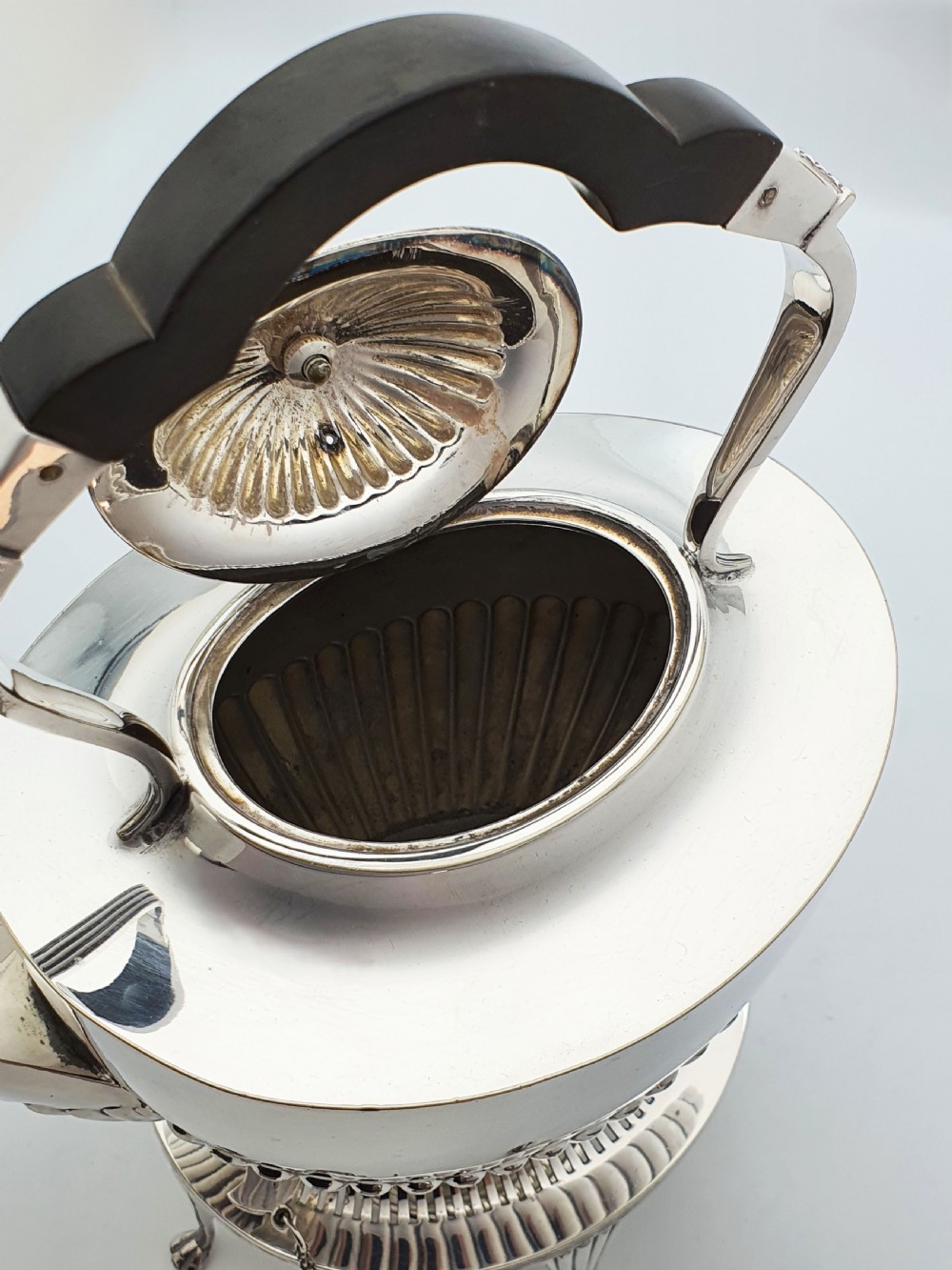 An Edwardian silver-plated spirit kettle featuring a half-fluted lower body, an ebony handle grip, and a matching tripod stand with an alcohol burner. View VIII