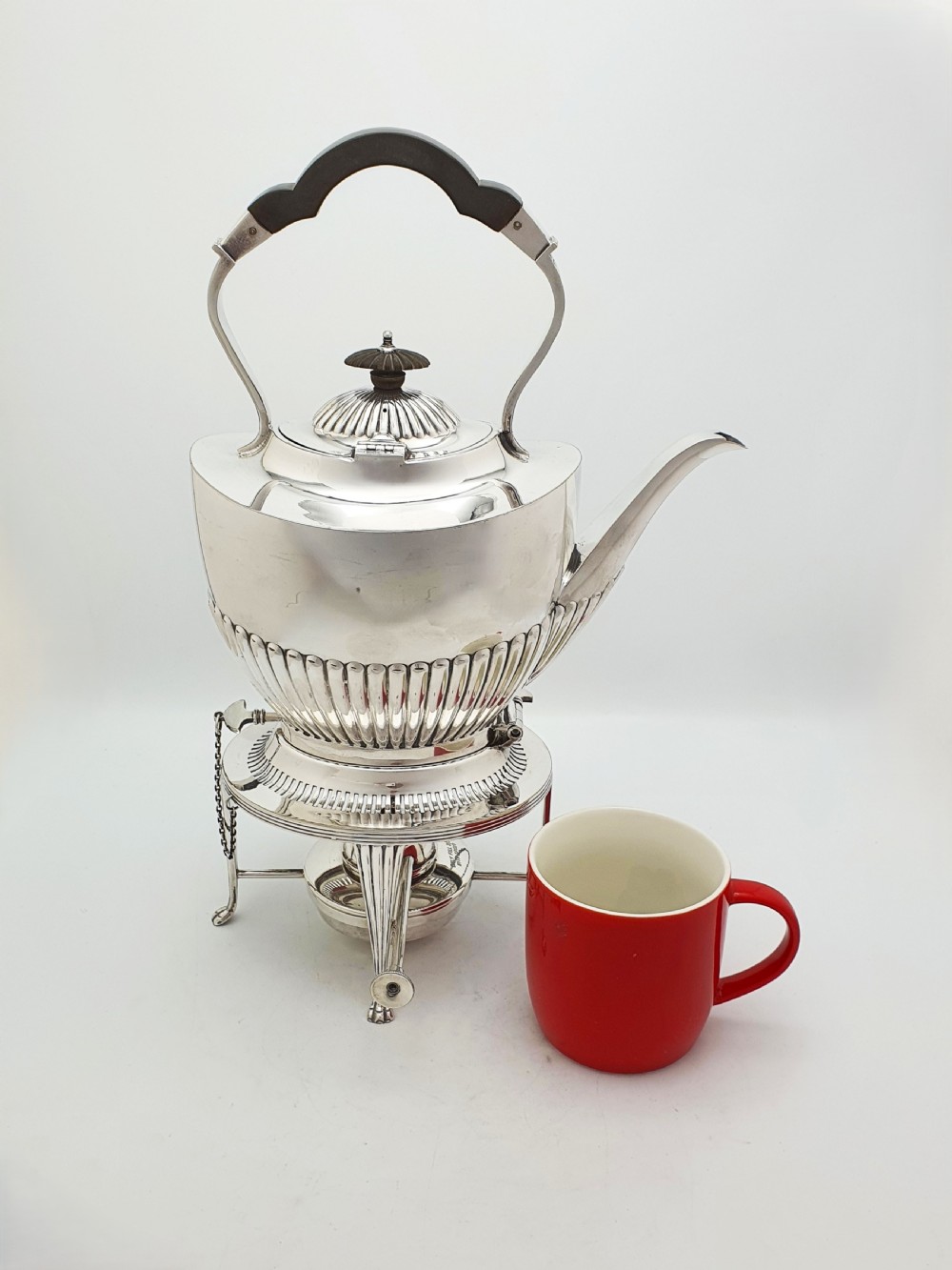 An Edwardian silver-plated spirit kettle featuring a half-fluted lower body, an ebony handle grip, and a matching tripod stand with an alcohol burner. View IX