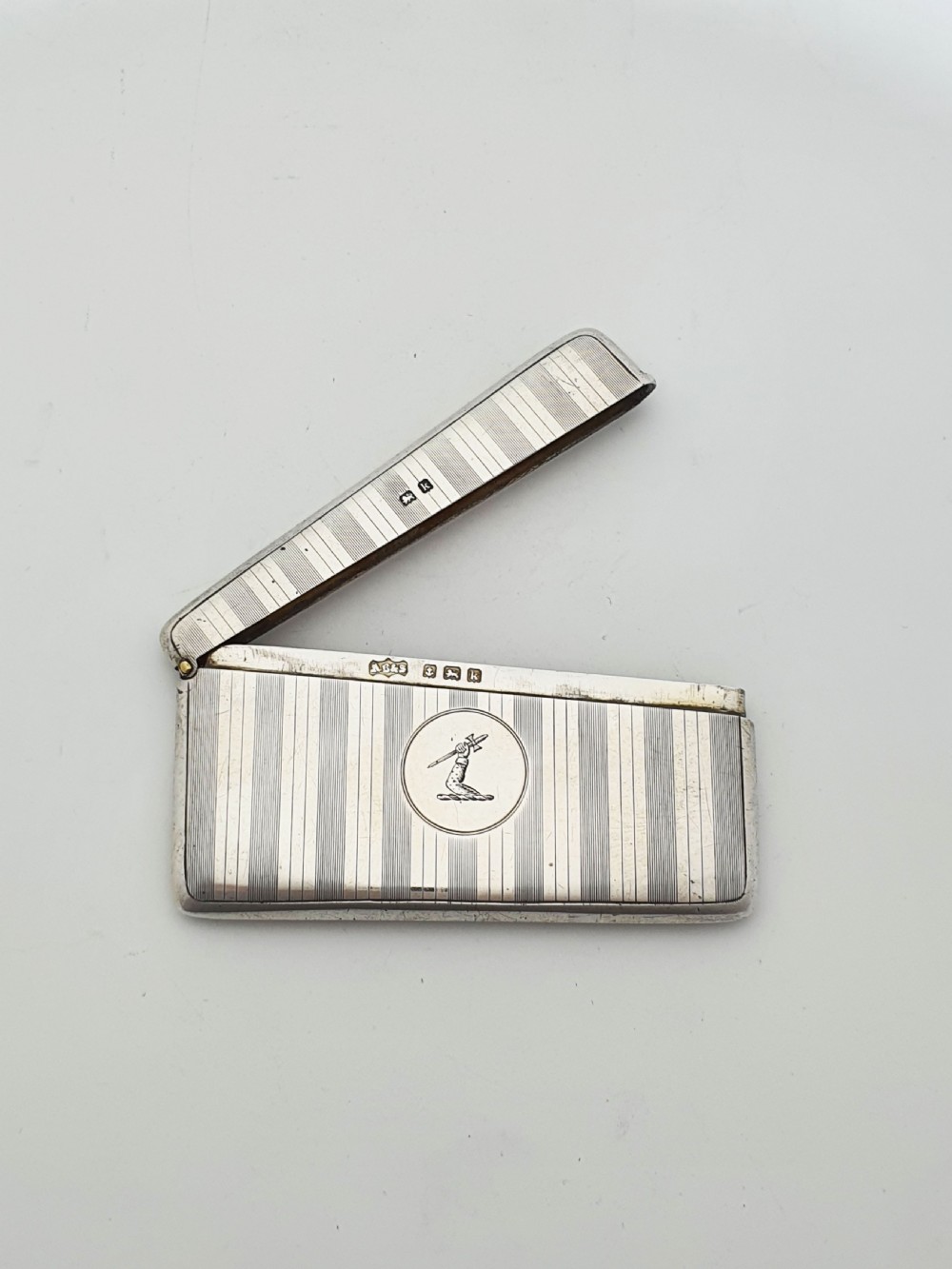 An open Edwardian sterling silver card box featuring an engine-turned striped pattern, British hallmarks, and an engraved central crest.