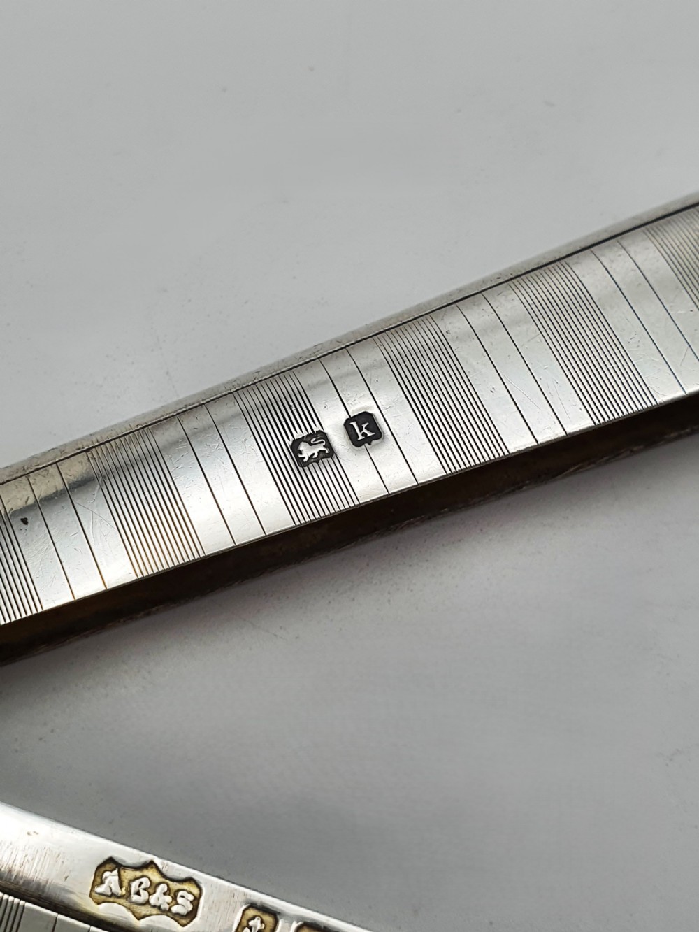 An open Edwardian sterling silver card box featuring an engine-turned striped pattern, British hallmarks, and an engraved central crest. View V