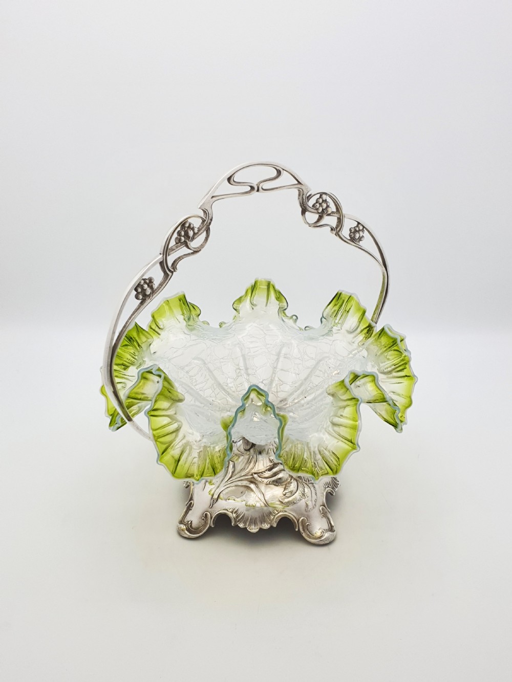An Art Nouveau silver-plated centrepiece frame with an arched handle holding a frilled green-rimmed vaseline glass dish with a crackle texture. View II