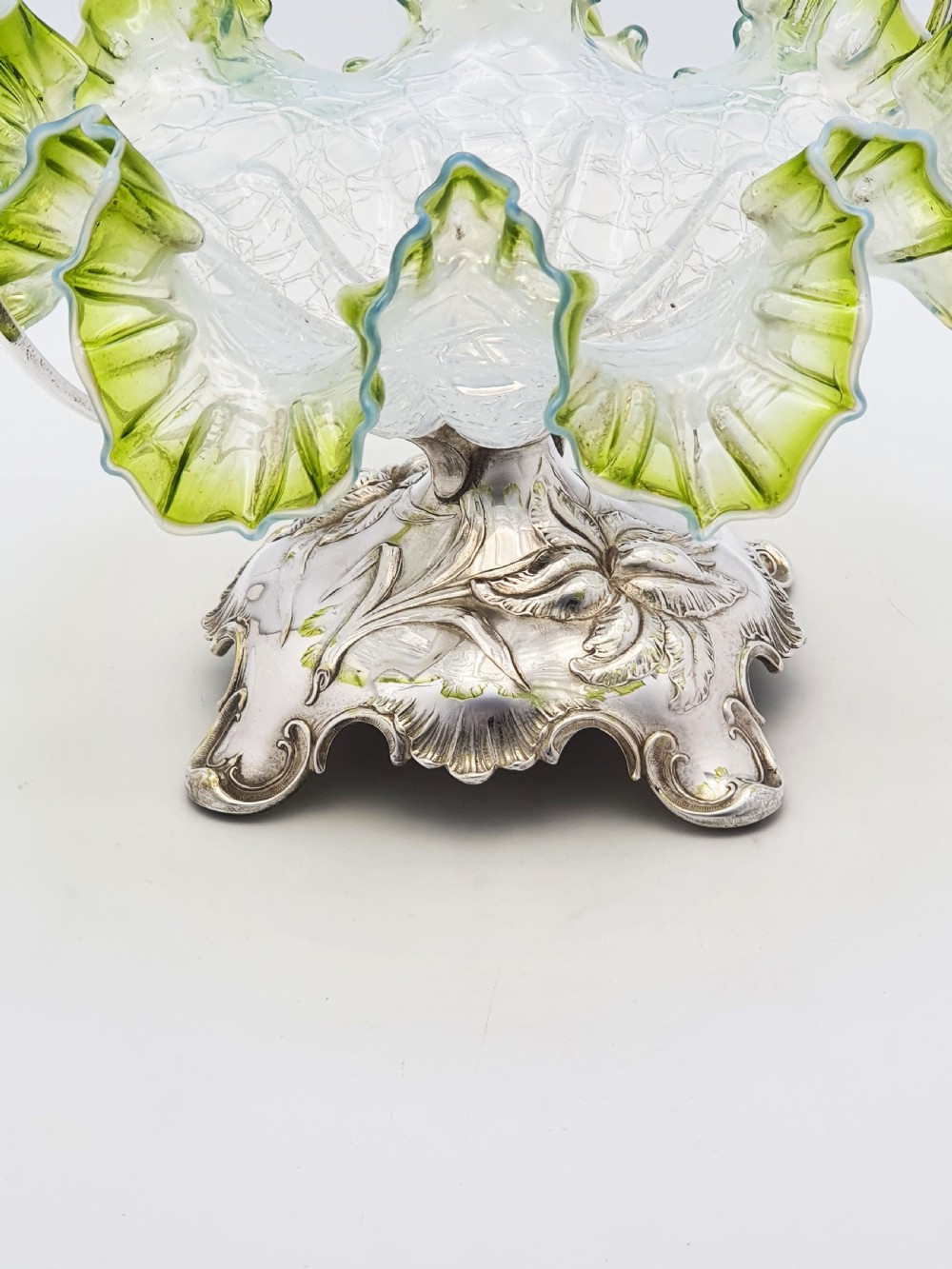An Art Nouveau silver-plated centrepiece frame with an arched handle holding a frilled green-rimmed vaseline glass dish with a crackle texture. View IV