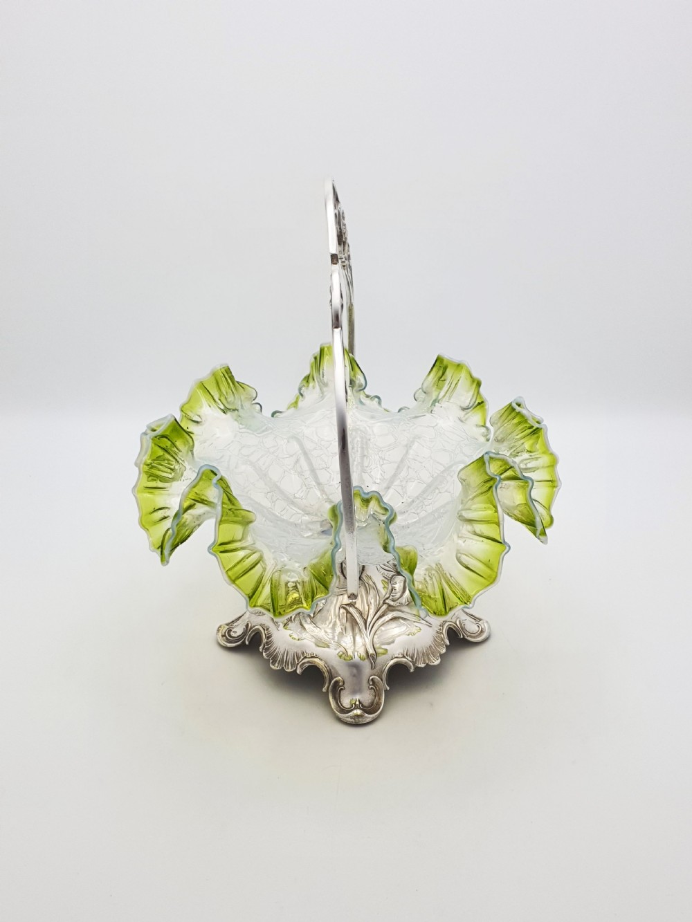 An Art Nouveau silver-plated centrepiece frame with an arched handle holding a frilled green-rimmed vaseline glass dish with a crackle texture. View V