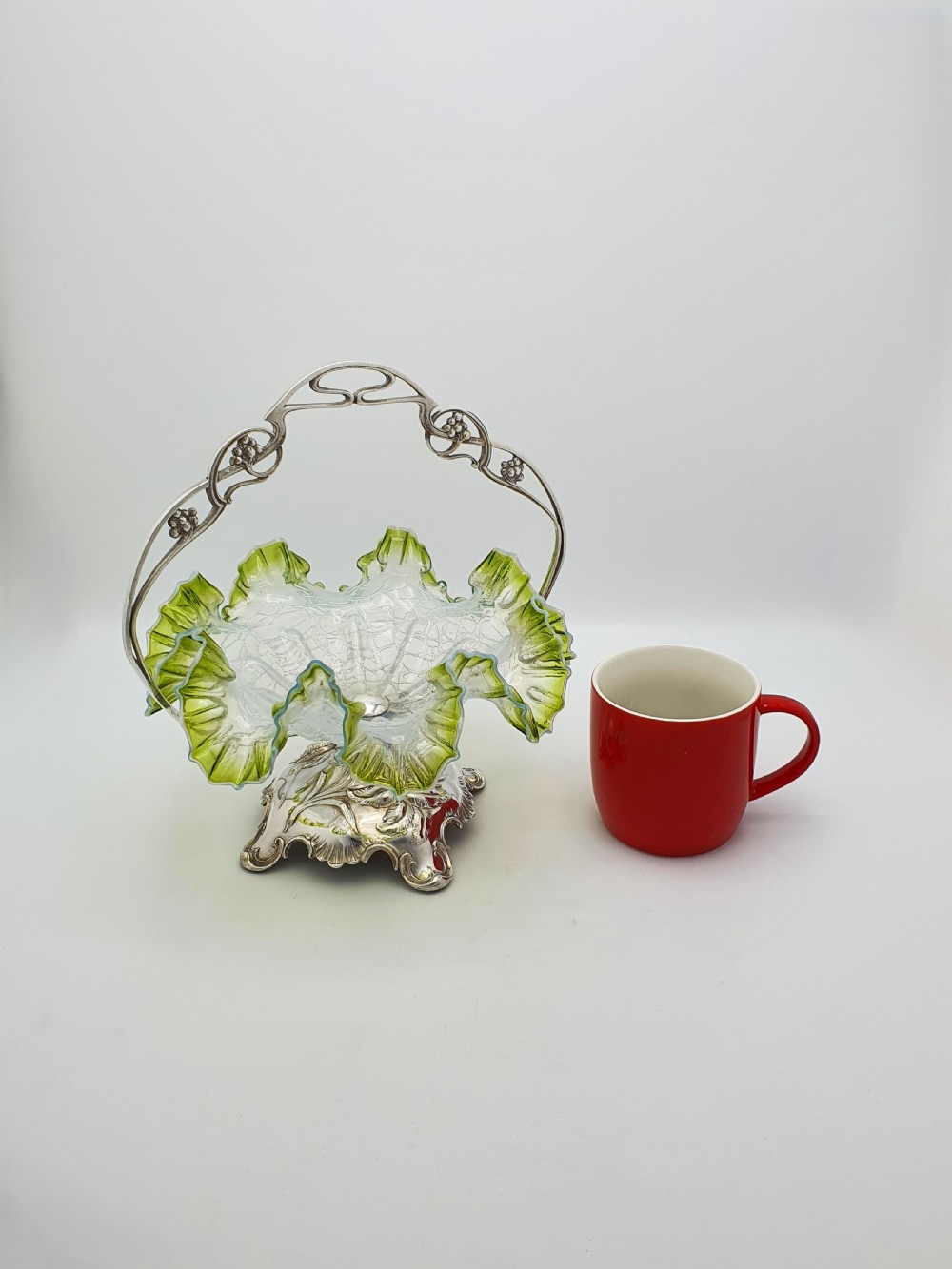 An Art Nouveau silver-plated centrepiece frame with an arched handle holding a frilled green-rimmed vaseline glass dish with a crackle texture. View VIII