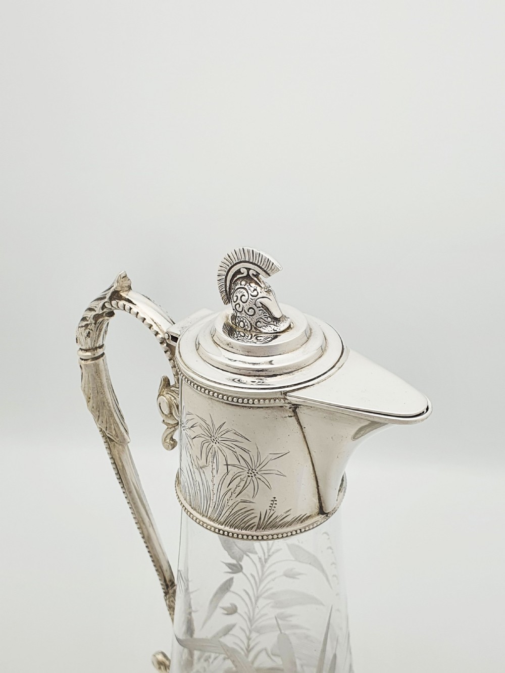 A Victorian etched clear glass claret jug featuring botanical engravings and a silver-plated handle, spout, and helmet finial. View II