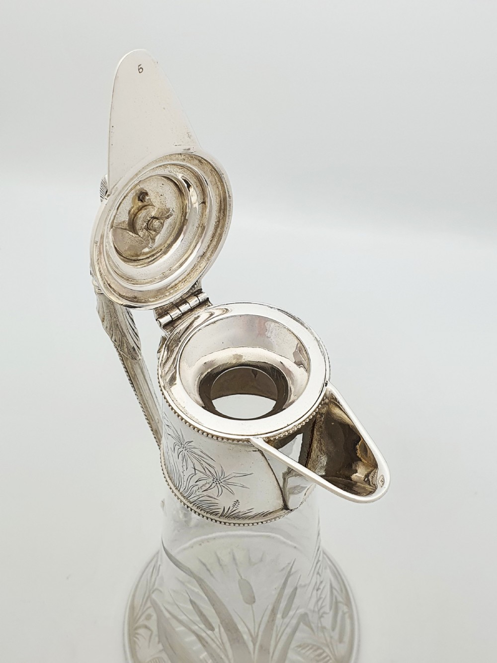 A Victorian etched clear glass claret jug featuring botanical engravings and a silver-plated handle, spout, and helmet finial. View V