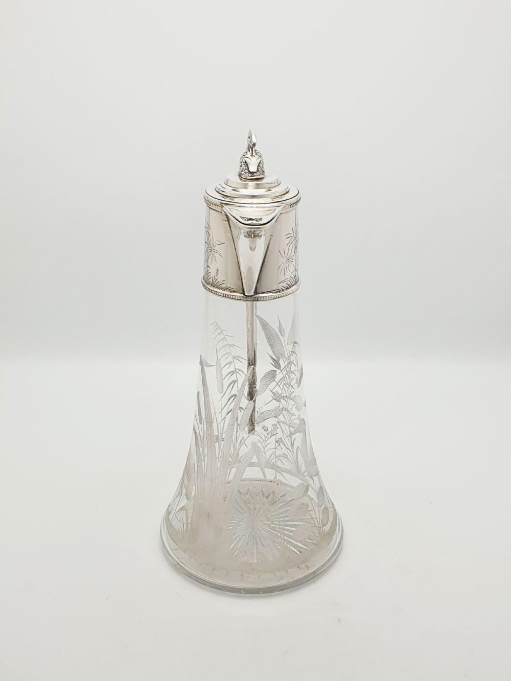 A Victorian etched clear glass claret jug featuring botanical engravings and a silver-plated handle, spout, and helmet finial. View VII