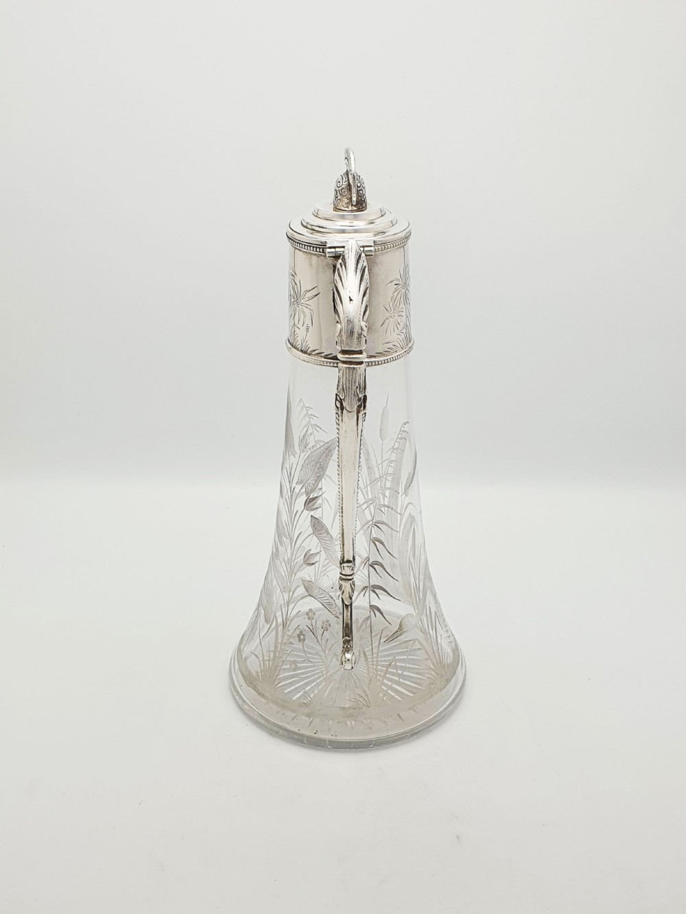 A Victorian etched clear glass claret jug featuring botanical engravings and a silver-plated handle, spout, and helmet finial. View IX