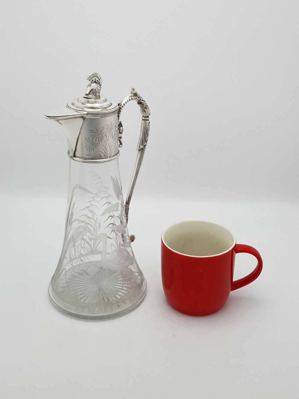 A Victorian etched clear glass claret jug featuring botanical engravings and a silver-plated handle, spout, and helmet finial. View X
