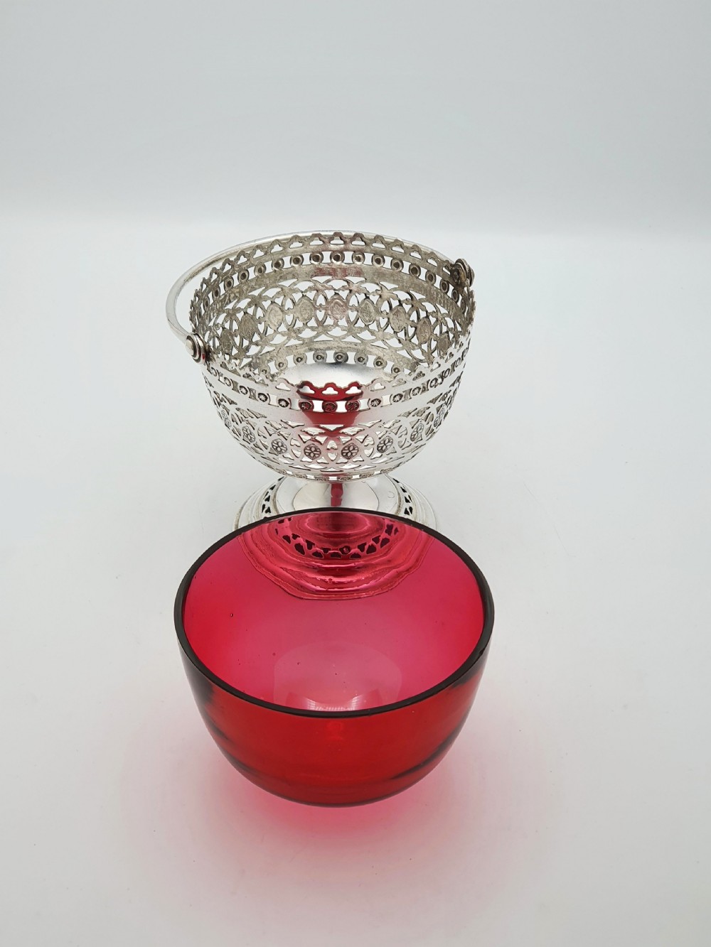 An Edwardian silver-plated footed basket featuring pierced geometric fretwork, a swing handle, and a removable ruby red glass liner. View IV
