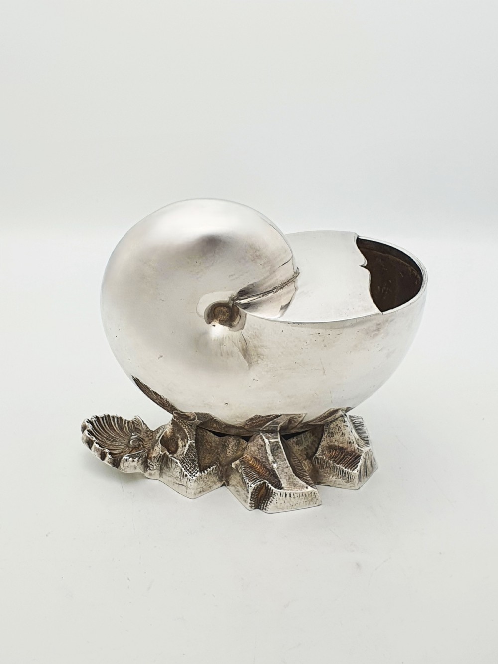 A Victorian silver-plated spoon warmer designed in the form of a nautilus shell mounted on a textured rocky base. View II