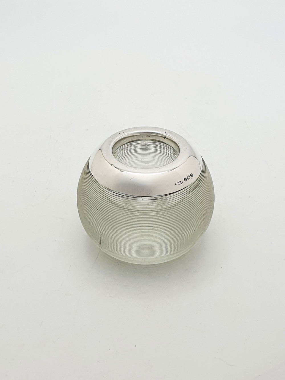 A spherical clear ribbed glass match striker featuring a hallmarked sterling silver collar around the top rim.