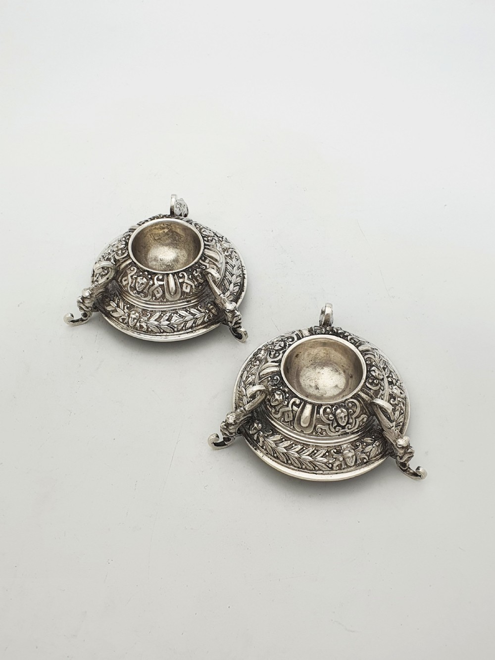 A pair of Victorian sterling silver salt cellars decorated with chased classical masks, foliate wreaths, and tripod feet. View II