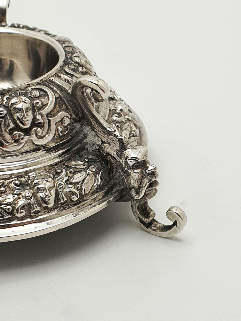 A pair of Victorian sterling silver salt cellars decorated with chased classical masks, foliate wreaths, and tripod feet. View IV