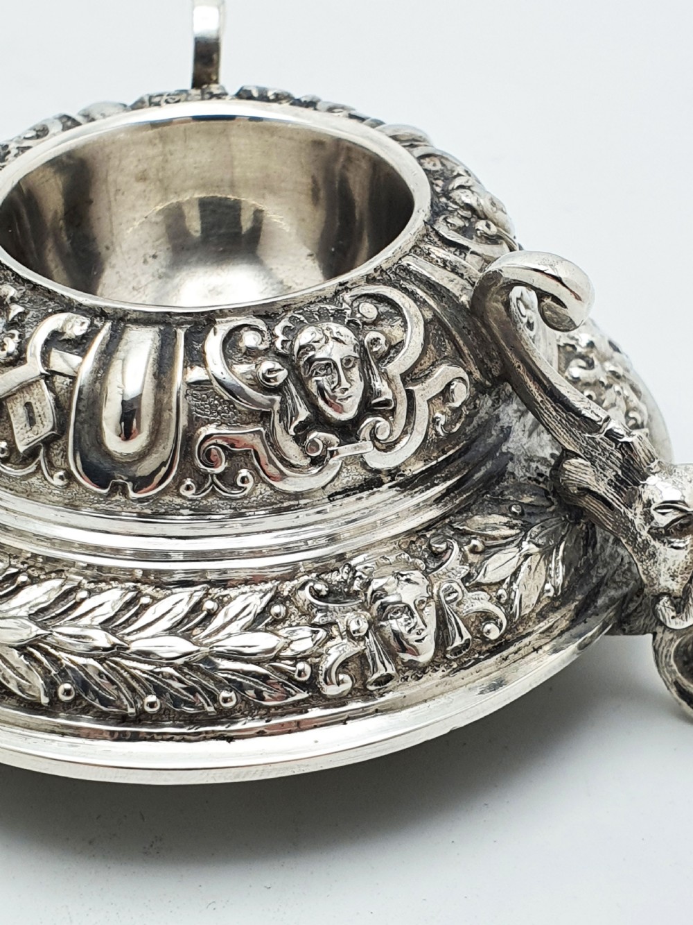 A pair of Victorian sterling silver salt cellars decorated with chased classical masks, foliate wreaths, and tripod feet. View V