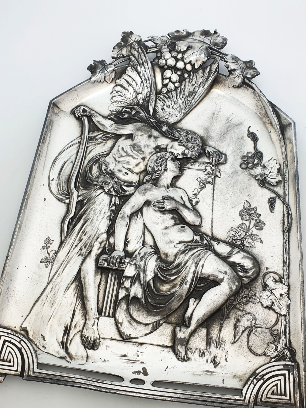 An arched silver-plated metal relief wall plaque featuring a classical mythological figure scene framed by grapevines and geometric motifs. View III