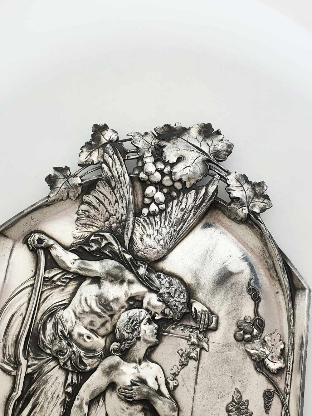 An arched silver-plated metal relief wall plaque featuring a classical mythological figure scene framed by grapevines and geometric motifs. View IV